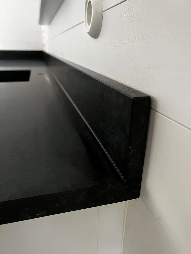 Närbild av den L-formade anslutningen i matt Nero Assoluto granit med stänkkant mot vit vägg i Åhus.