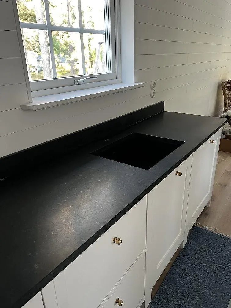 L-formad köksbänkskiva i matt Nero Assoluto granit med svart diskho, vita luckor och takfönster i Åhus.