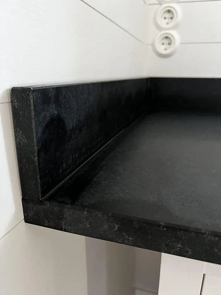 Detalj av uppvikt stänkkant och hörn i matt Nero Assoluto granit vid ljus vägg i Åhus.
