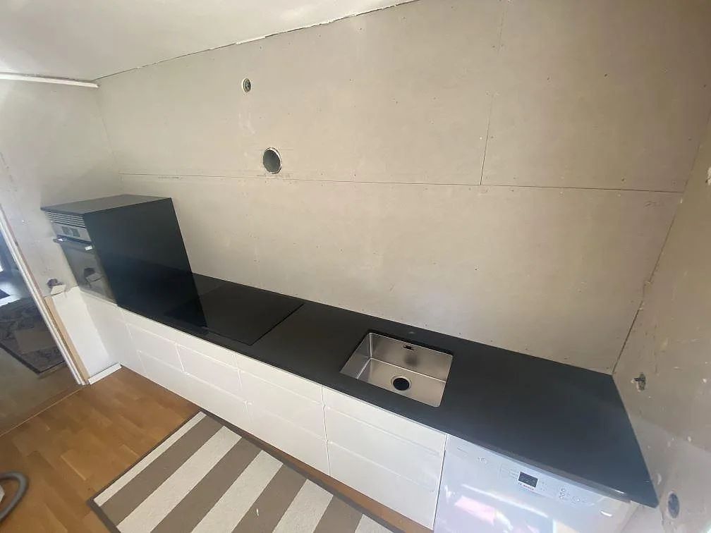 Köksbänkskiva i svart Nero Assoluto granit, polerad, med underlimmad rostfri diskho och infälld induktionshäll längs en hel köksrad i ett kök i Åkarp.