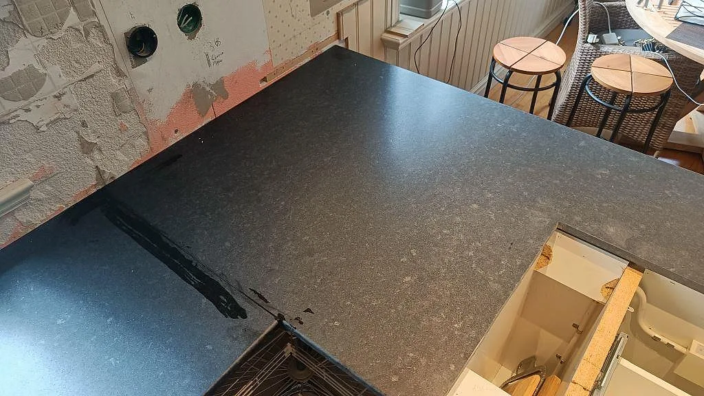 Bänkskiva i matt Nero Assoluto granit sedd uppifrån mot bar vägg under montering i ett kök i Ängelholm.