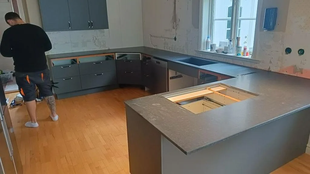Köksbänkskiva i matt svart granit Nero Assoluto, U-formad med halvö, i ett kök under montering i Ängelholm.
