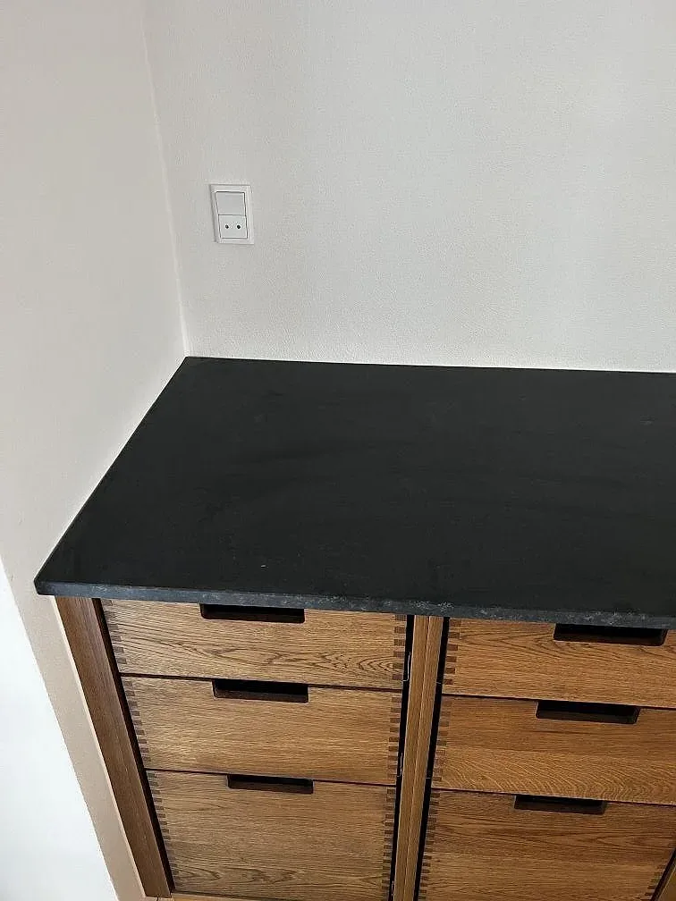 Rak köksbänkskiva i matt Nero Assoluto granit mot vit vägg och träskåp i Assens.