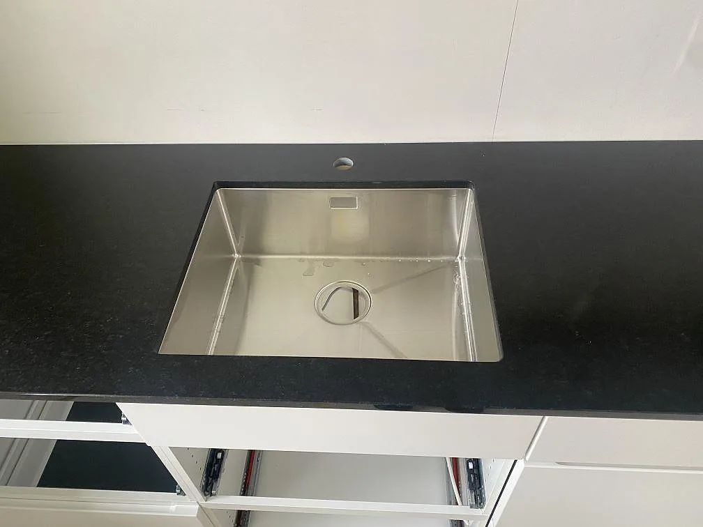 Närbild på underlimmad rostfri diskho i en matt Nero Assoluto bänkskiva av granit i Båstad.