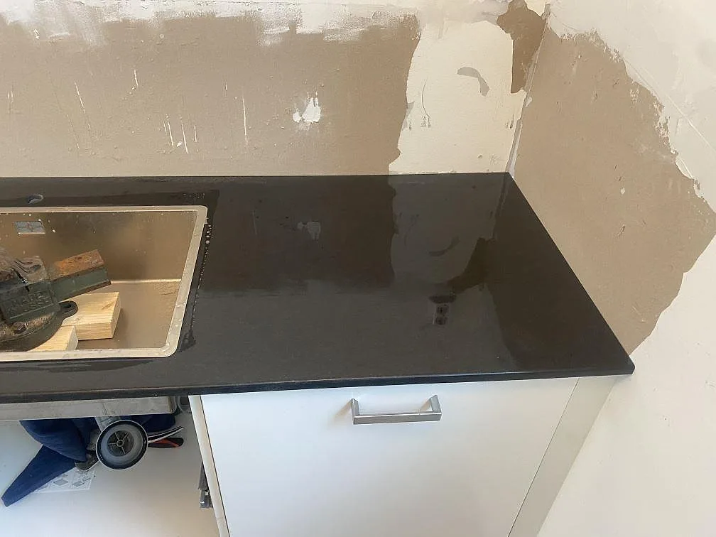 Köksbänkskiva i svart Nero Assoluto granit vid diskhon och hörnet på vita stommar i Båstad.