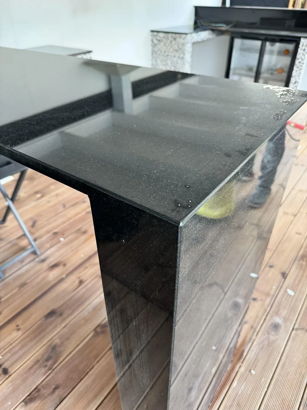 Närbild av polerad Nero Assoluto granit med lodrät stensida och speglingar från trätrallen i Bara.