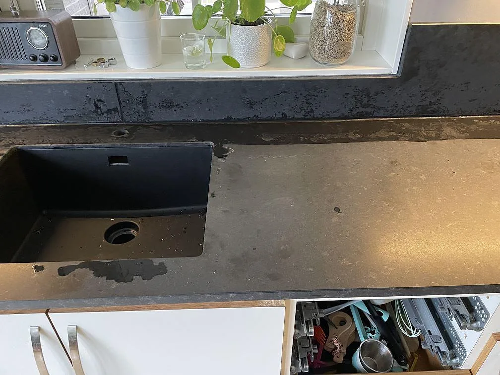 Köksbänkskiva i matt svart granit Nero Assoluto med underlimmad svart kompositdiskho under fönstret i ett kök i Bjuv.