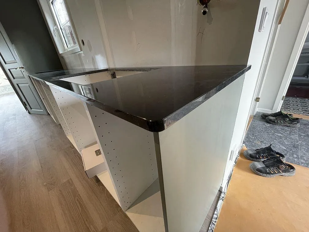 Köksbänkskiva i polerad svart Nero Assoluto-granit med L-format hörn och urtag för diskho, monterad i ett kök under montering i Borlänge.