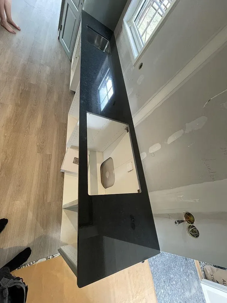 Lång köksbänkskiva i polerad Nero Assoluto-granit sedd ovanifrån, med urtag för diskho och häll, monterad på öppna köksstommar i Borlänge.