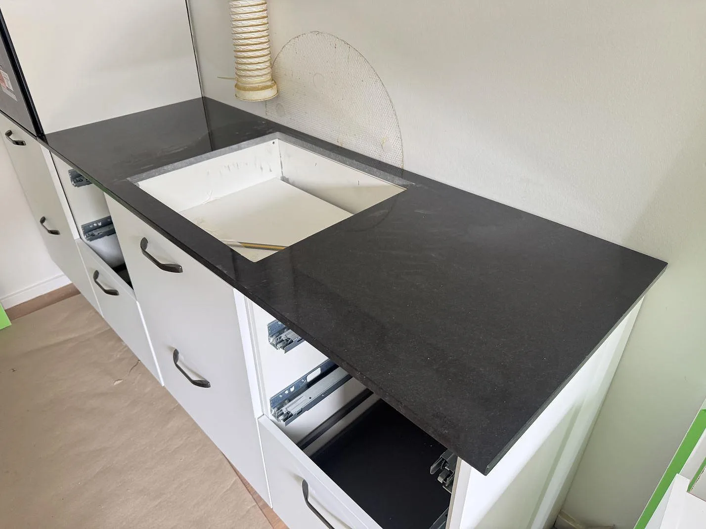 Köksbänkskiva i polerad Nero Assoluto granit med urtag för häll i ett vitt kök under montering i Bröndby.
