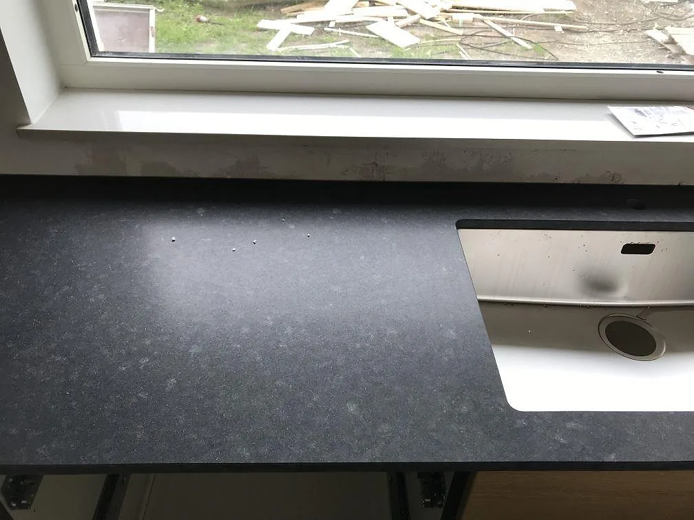 Underlimmad rostfri diskho i en köksbänkskiva av matt svart granit, Nero Assoluto, vid fönstret i ett kök i Bunkeflostrand.