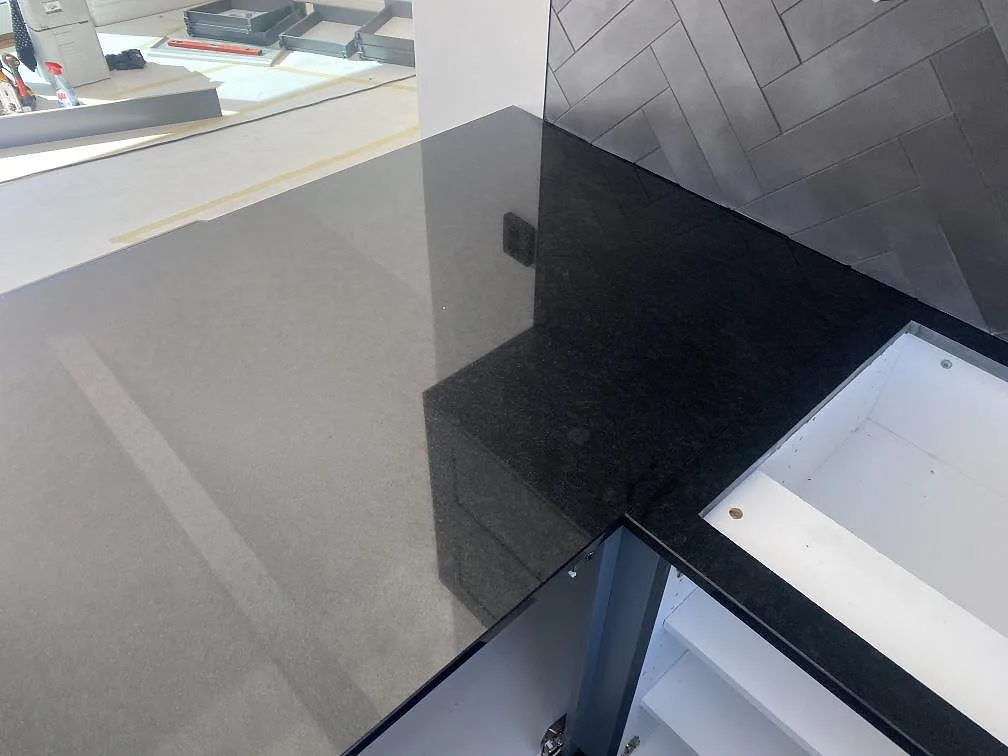 Top-down vy av installerad polerad Nero Assoluto granitbänkskiva mot fiskbensmönstrat stänkskydd i ett kök i Bunkeflostrand.