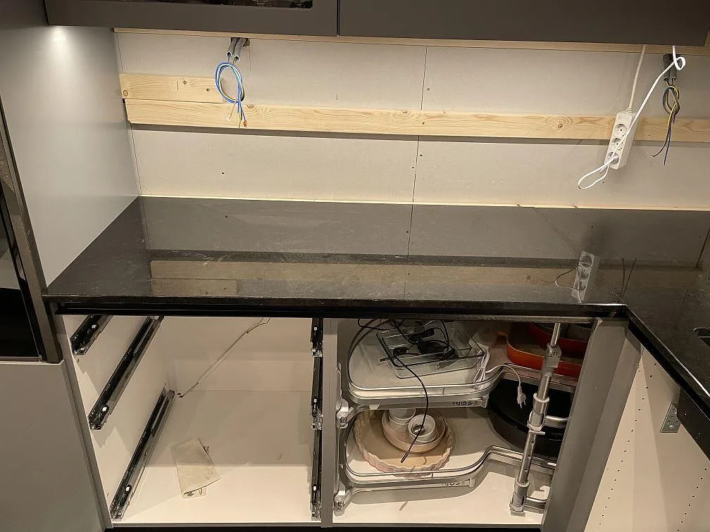 Rak köksbänk i polerad Nero Assoluto granit på vita stommar under väggskåp i Dalby.