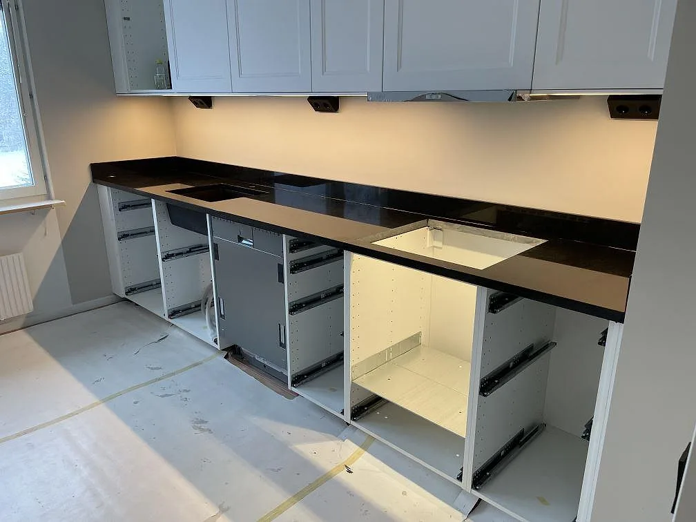 Köksbänkskiva i polerad svart granit Nero Assoluto, med underlimmad diskhoplacering och plats för häll, monterad i ett kök i Eskilstuna under installation.