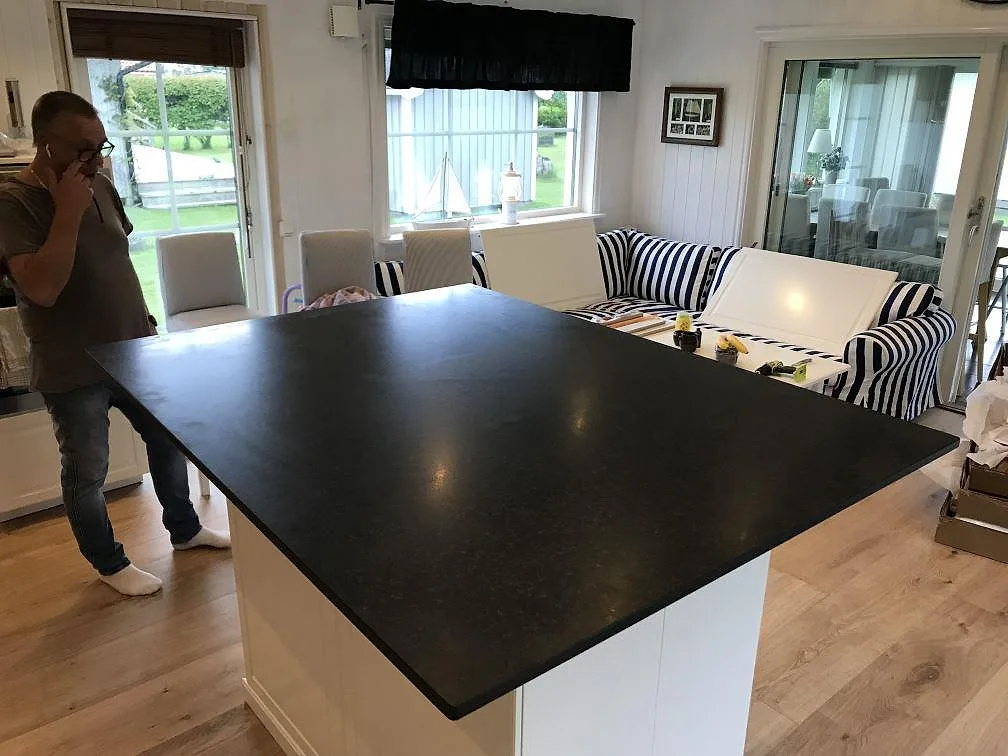 Köksö i matt svart Nero Assoluto-granit, 20 mm, monterad på vit stomme i ett ljust kök med öppen planlösning i Falkenberg.