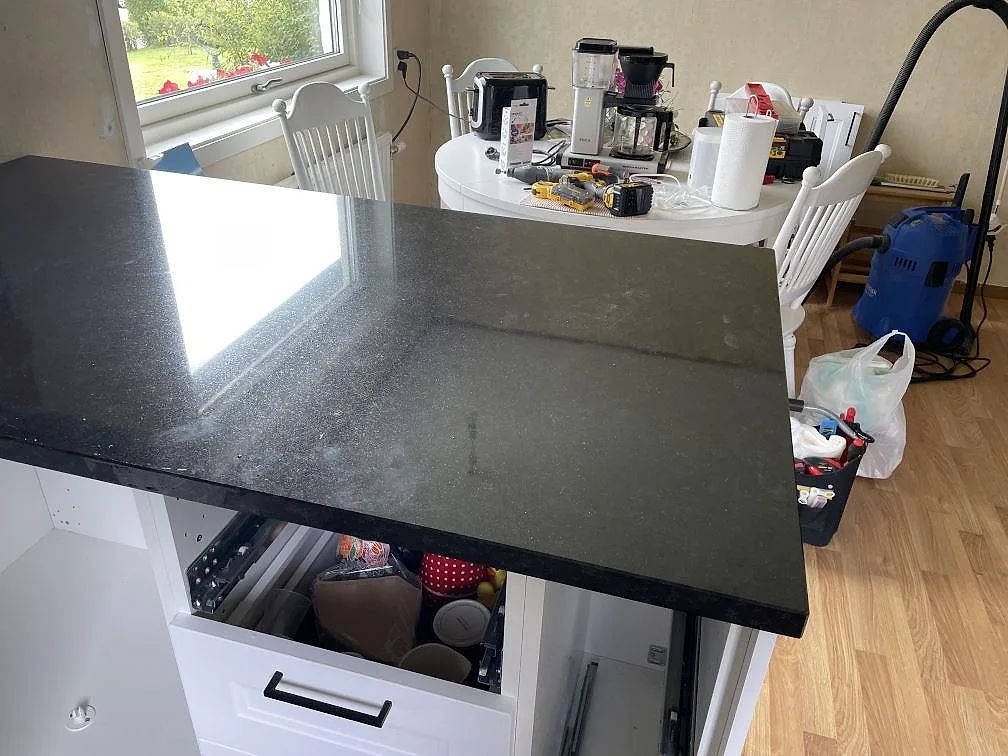 Polerad köksbänkskiva i svart Nero Assoluto granit på en halvö med vit skåpsinredning i Falkenberg.