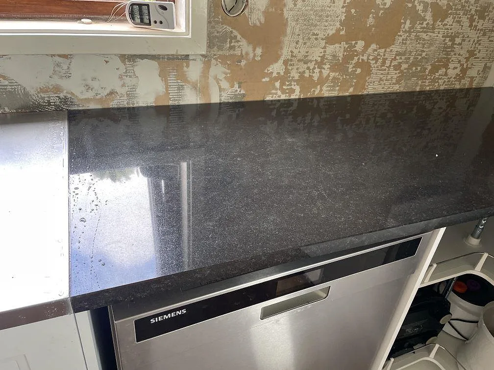 Rak bänkrad i polerad Nero Assoluto granit ovanför diskmaskin och öppna köksstommar i Falkenberg.