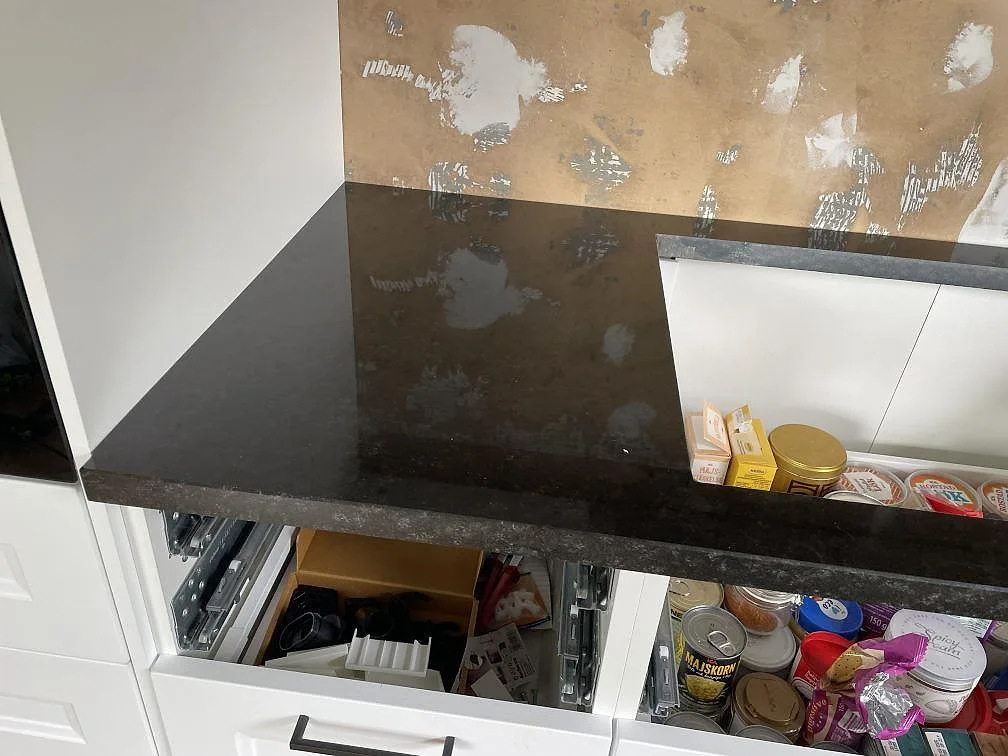 Detalj av polerad svart Nero Assoluto granit monterad över öppna vita skåp i kök i Falkenberg.