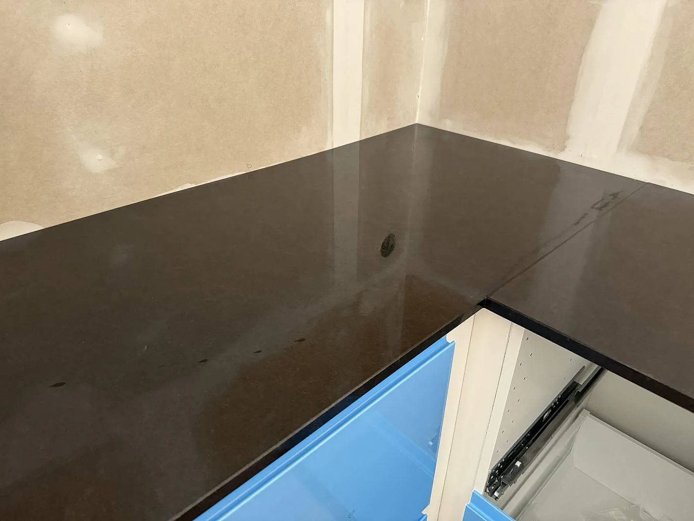 Hörnvy av polerad Nero Assoluto granitbänkskiva över blå köksinredning och beige väggar i Falköping.