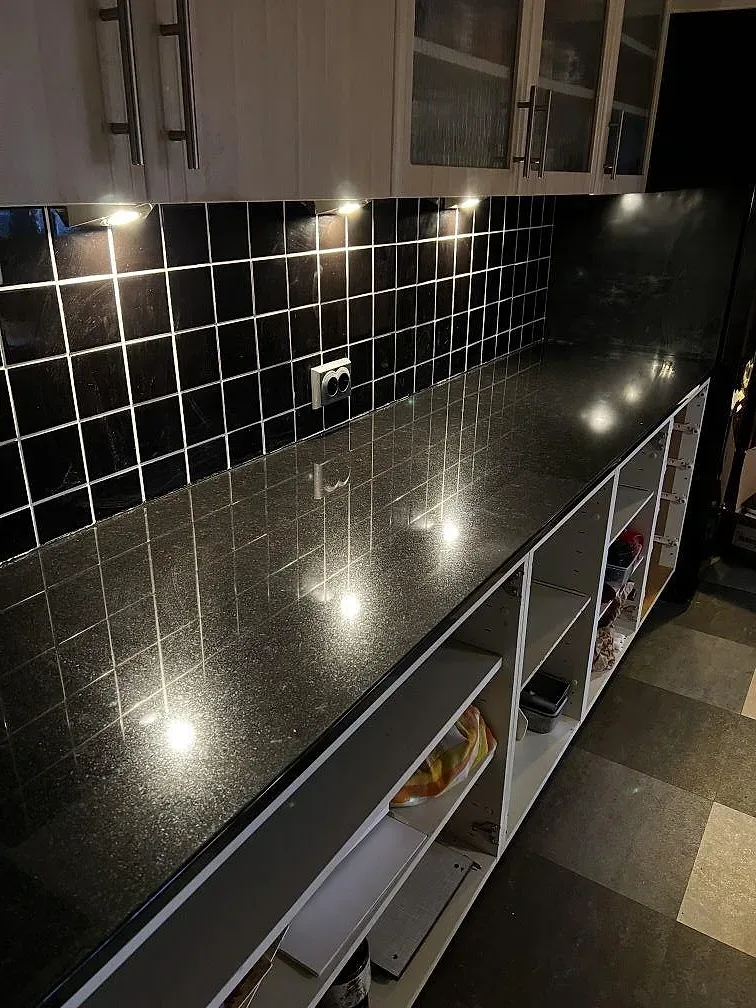 L-formad köksbänk i polerad Nero Assoluto-granit med reflekterande spotlights och svart stänkskydd i ett kök under montering i Falsterbo.