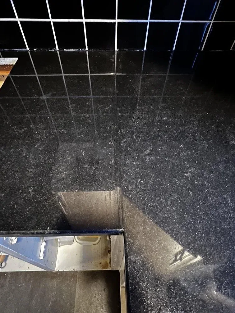 Närbild på polerad svart Nero Assoluto-granit som bänkskiva och stänkkant i ett kök i Falsterbo.