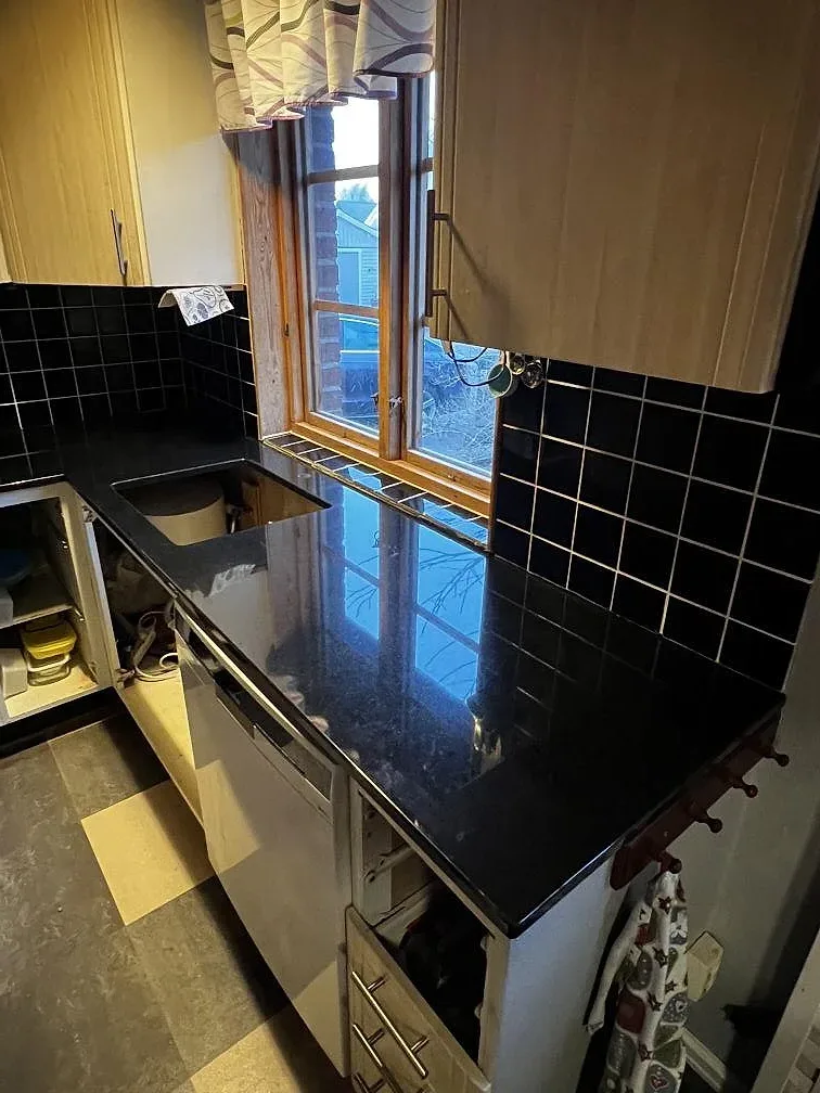 Köksbänk i svart Nero Assoluto-granit vid fönstret med svart kakel och granitbänk i ett kök i Falsterbo.
