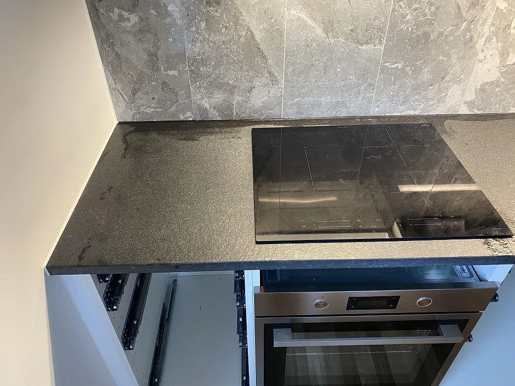 Detaljbild av matt Nero Assoluto Flamed and Brushed granit runt svart häll i ett kök i Limhamn.
