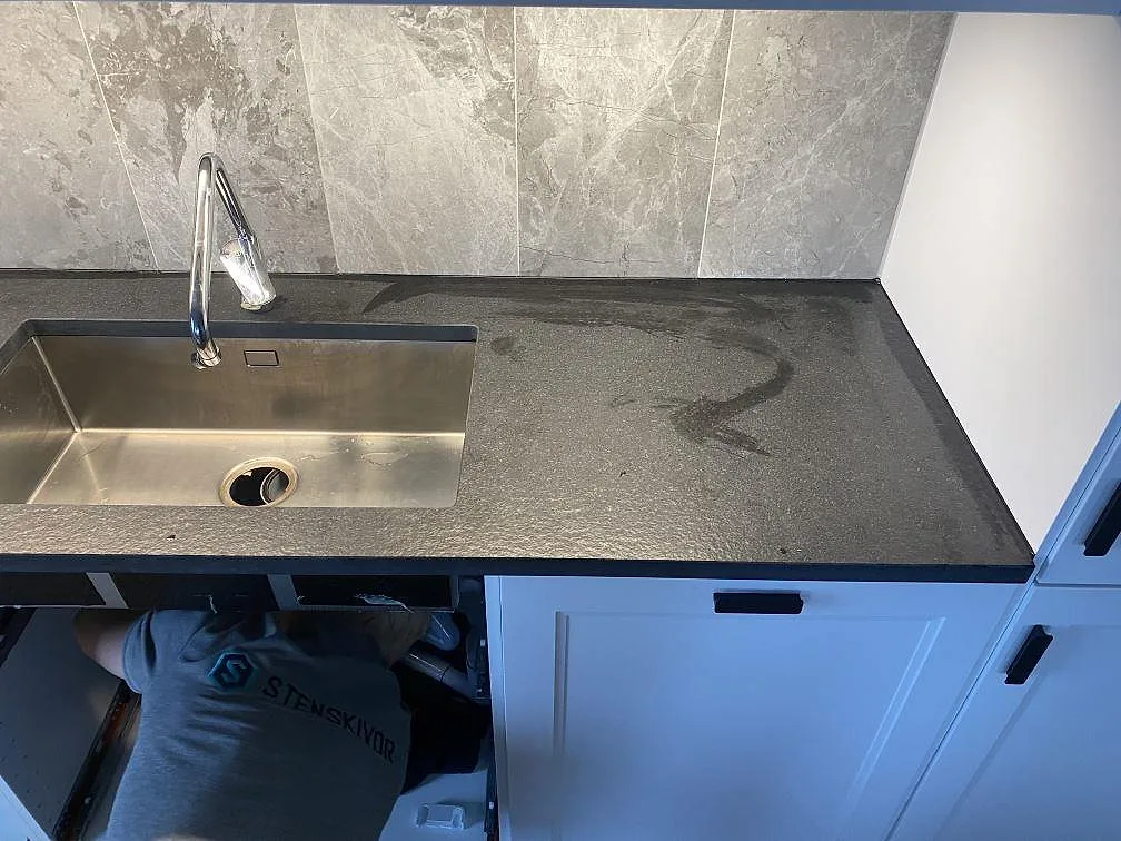 Mörk granitbänkskiva i matt Nero Assoluto Flamed and Brushed med rostfri diskho i ett vitt kök i Limhamn.