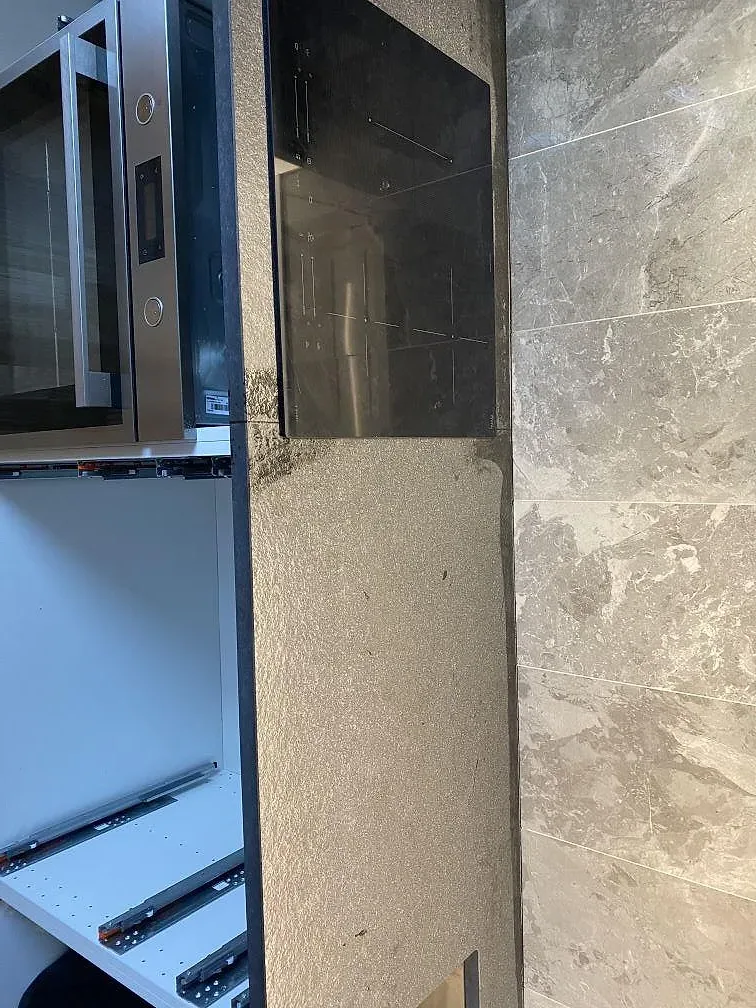 Köksbänkskiva i matt Nero Assoluto granit med infälld induktionshäll och ugn under montering i ett kök i Limhamn.