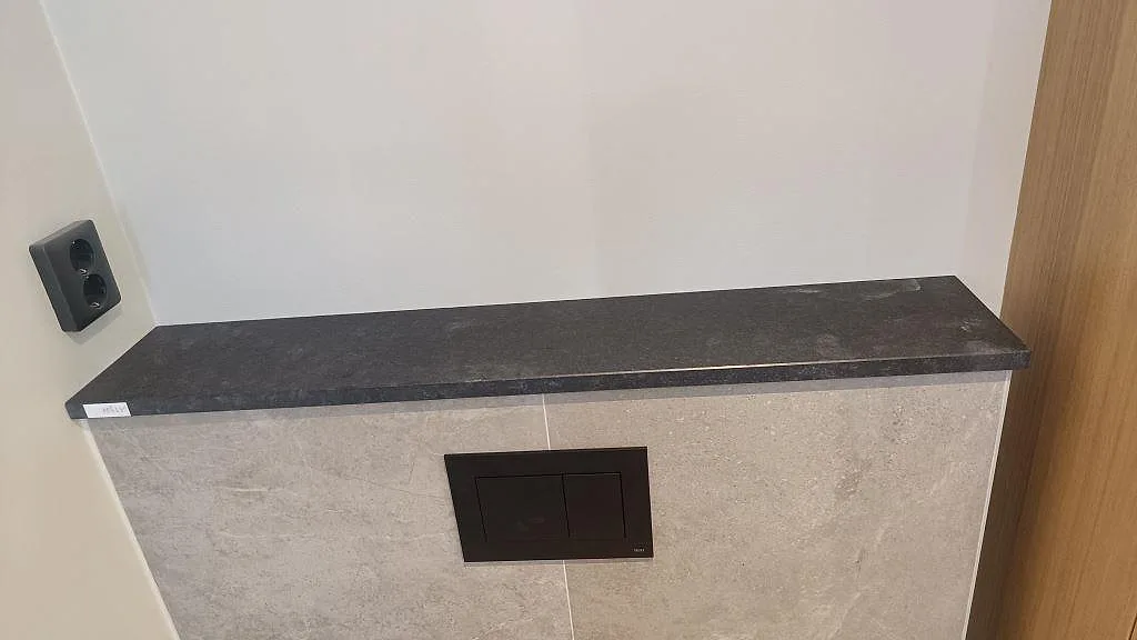 Installerad mörk bänkskiva i matt Nero Assoluto Flamed and Brushed granit på kaklad badrumsvägg i Mölndal.
