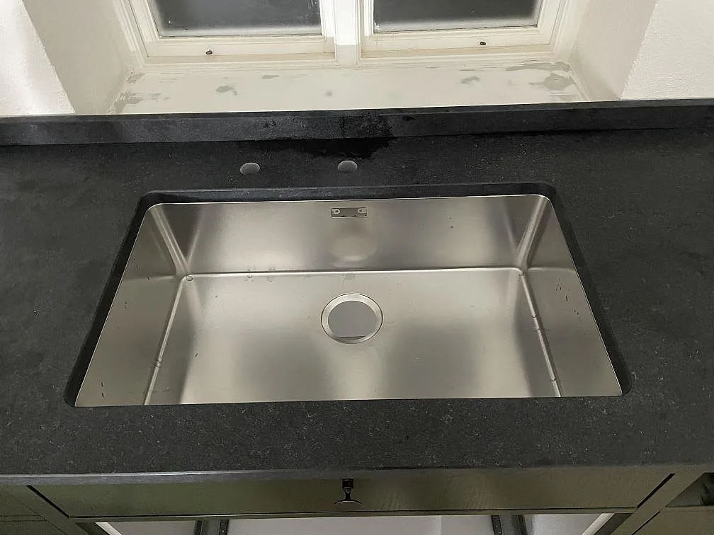 Underlimmad rostfri diskho i en matt svart granitbänkskiva av Nero Assoluto Flamed and Brushed i ett kök i Rydsgaard.