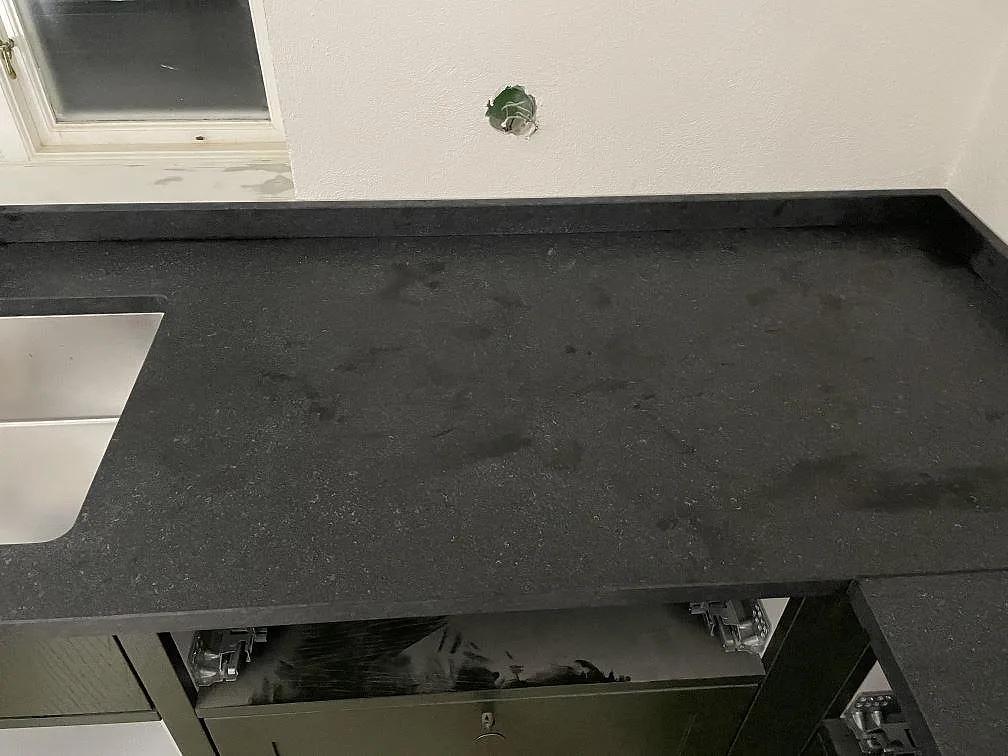 Matt lädrad yta på en köksbänkskiva i Nero Assoluto Flamed and Brushed med diskhohörn i ett kök i Rydsgaard.