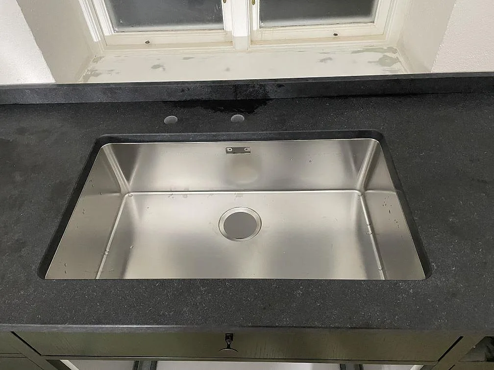 Stor underlimmad diskho i rostfritt stål i en flamed and brushed-bänkskiva av svart granit i ett kök i Rydsgaard.