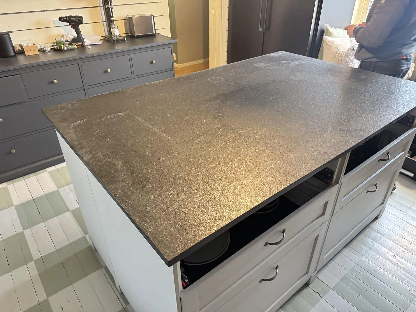 Bänkskiva på köksö i Nero Assoluto Flamed and Brushed granit, 20 mm matt yta, med mörka köksskåp i Vara.