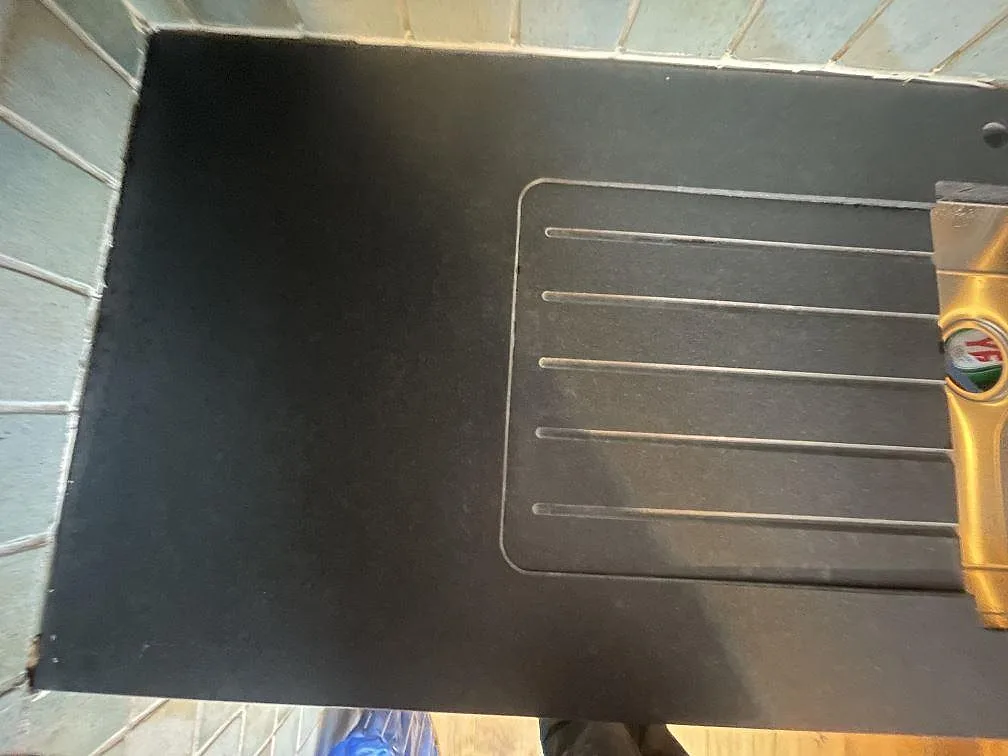 Närbild på det räfflade avrinningsplanet fräst i en matt svart Nero Assoluto bänkskiva mot grön kakel i ett kök i Frövi.