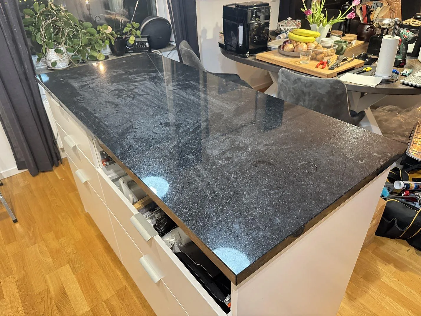 Köksö i polerad svart Nero Assoluto-granit med vita lådfronter i ett kök i Göteborg, med matplats och trägolv, fotograferad under montering.