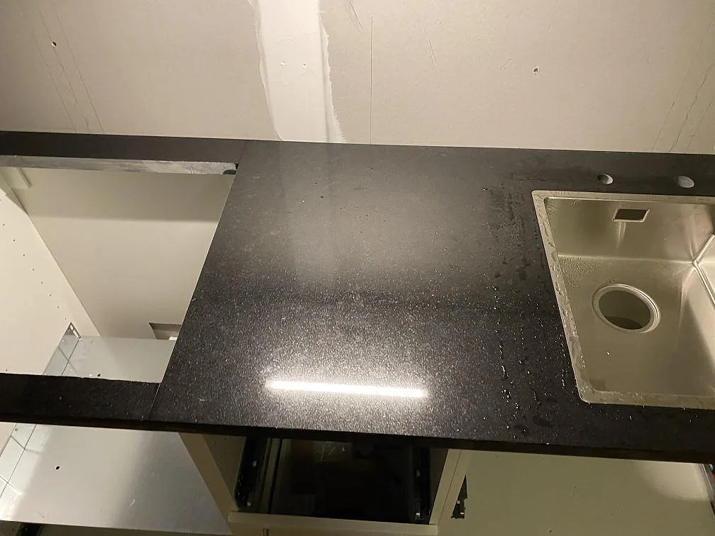Detalj av polerad Nero Assoluto granit vid diskhon, med svart arbetsyta och öppna köksstommar i Hässleholm.