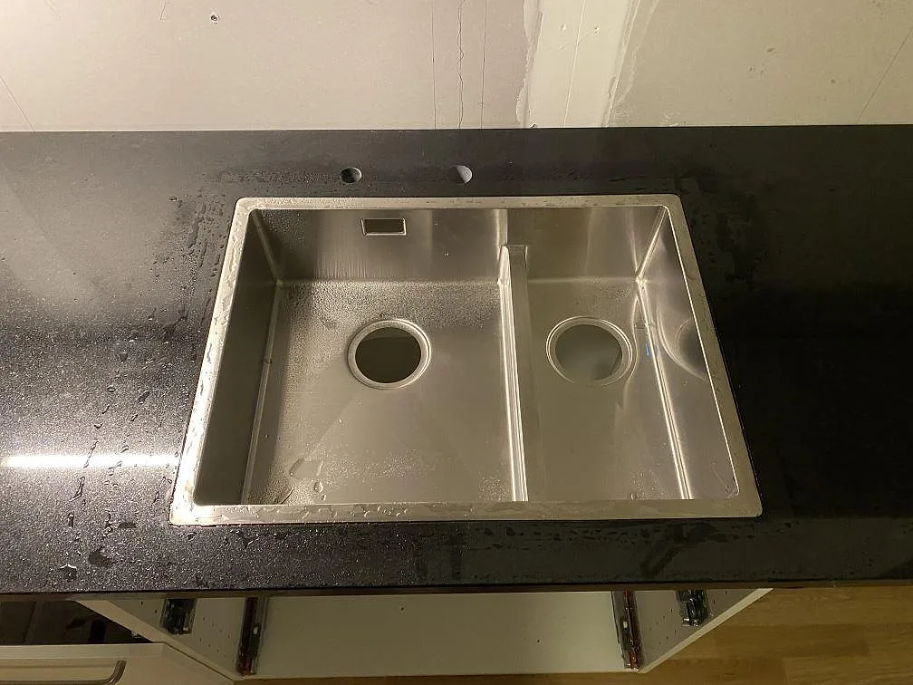 Närbild på polerad Nero Assoluto granit med rostfri dubbelho och kranhål i köket i Hässleholm.