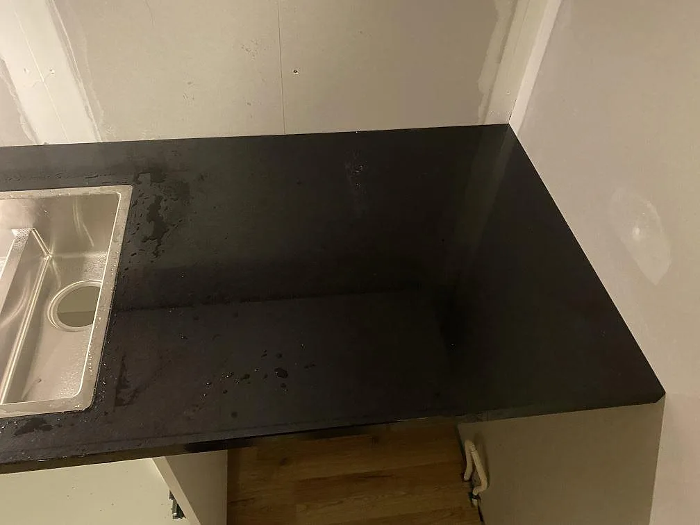 Höger arbetsyta i polerad Nero Assoluto granit bredvid diskhon i ett kök under montering i Hässleholm.