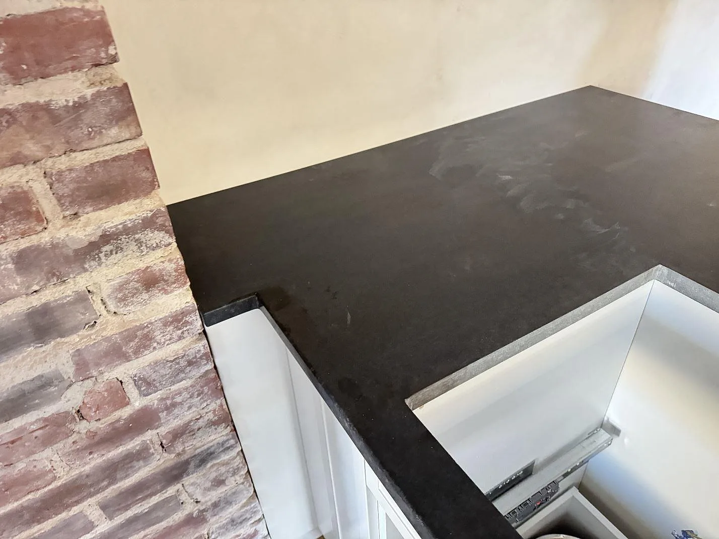 Installerad köksbänkskiva i matt svart Nero Assoluto-granit intill tegelmur och öppet urtag i Hässleholm.