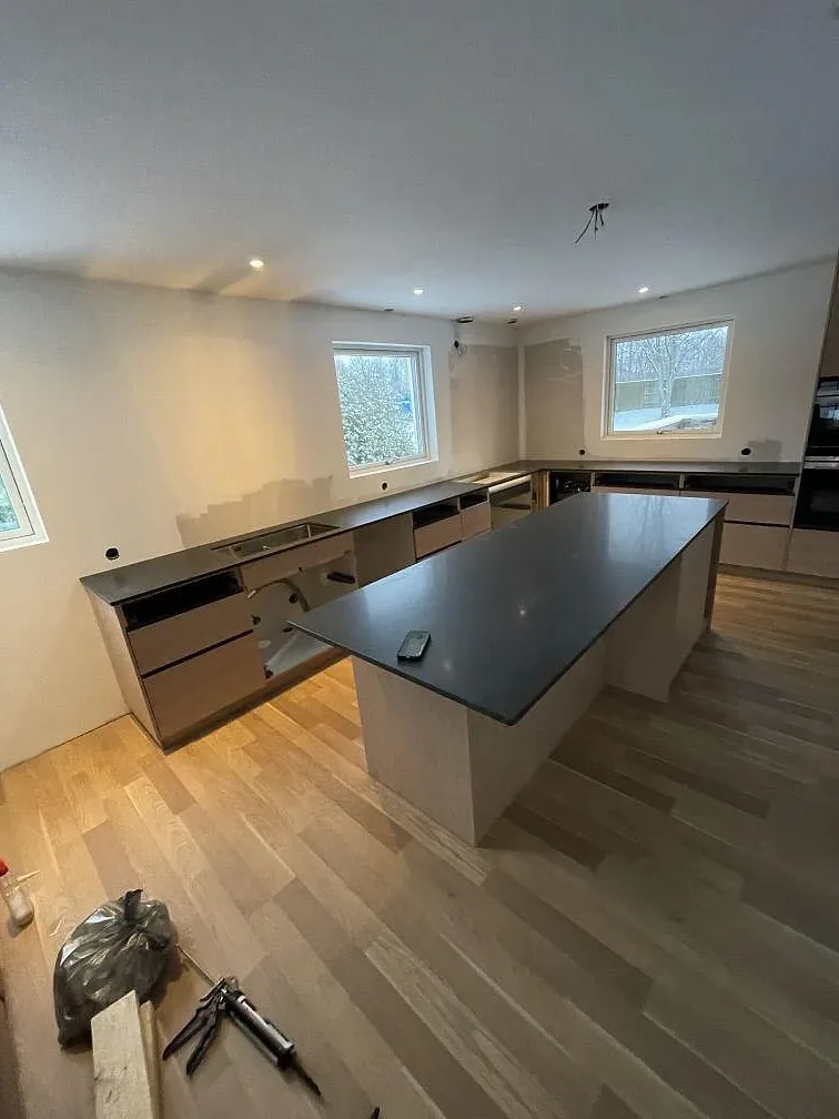 Köksö och bänkrad i matt svart Nero Assoluto granit i ett stort kök under montering i Halmstad