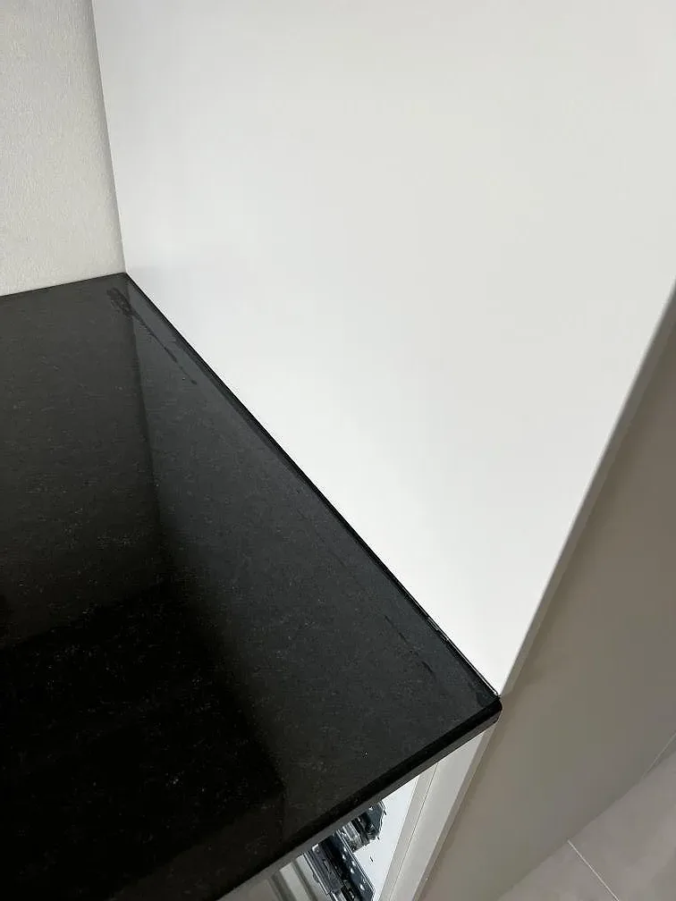 Närbild på blank svart Nero Assoluto granit mot vit vägg och köksinredning i Helsingborg.
