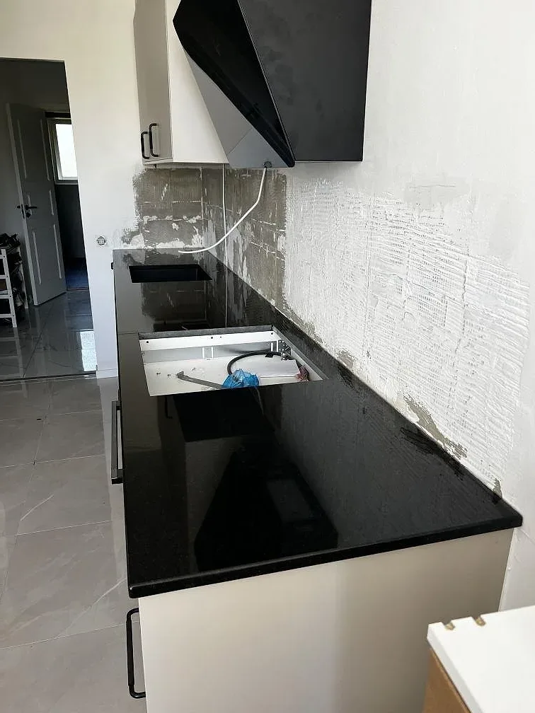Köksbänkskiva i svart Nero Assoluto granit, polerad, med L-formad halvö och öppna köksstommar i Helsingborg.