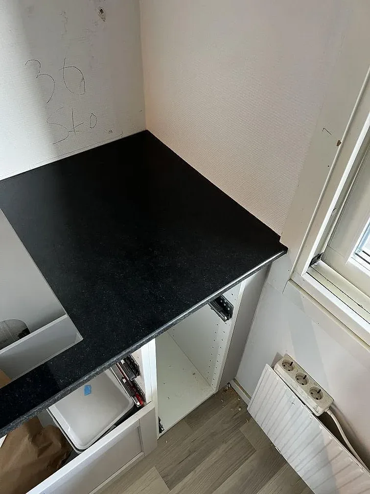 Polerad Nero Assoluto granit som lång köksbänkskiva vid fönster och vita köksstommar i Helsingborg.