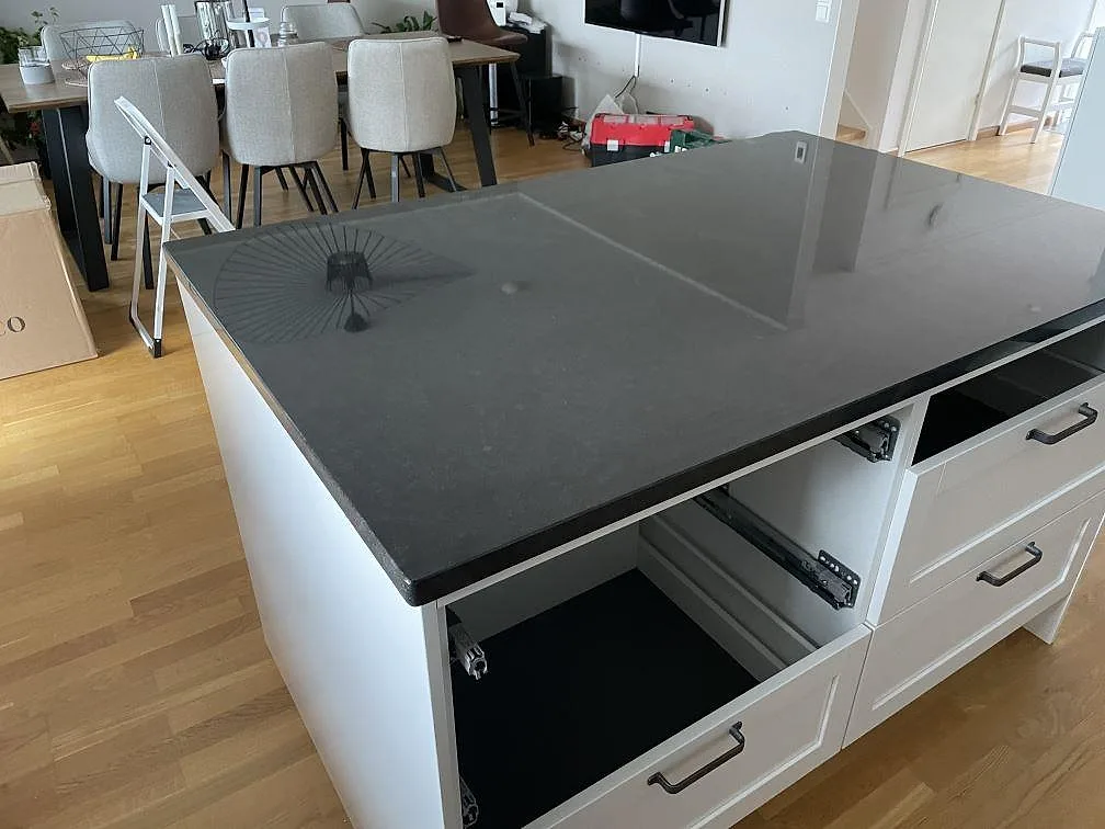 Närbild av polerad Nero Assoluto granit på köksö med öppna stommar och matplats bakom i Huskvarna.