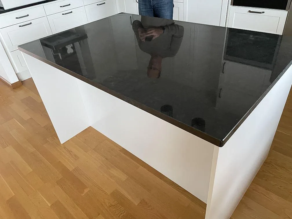 Blank svart köksöskiva i Nero Assoluto granit med speglingar, vita köksfronter och trägolv i Huskvarna.