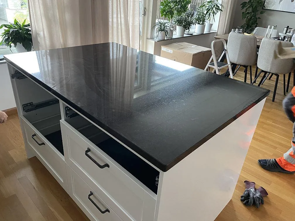 Polerad köksöskiva i Nero Assoluto granit på vit köksö under montering i ett öppet kök i Huskvarna.