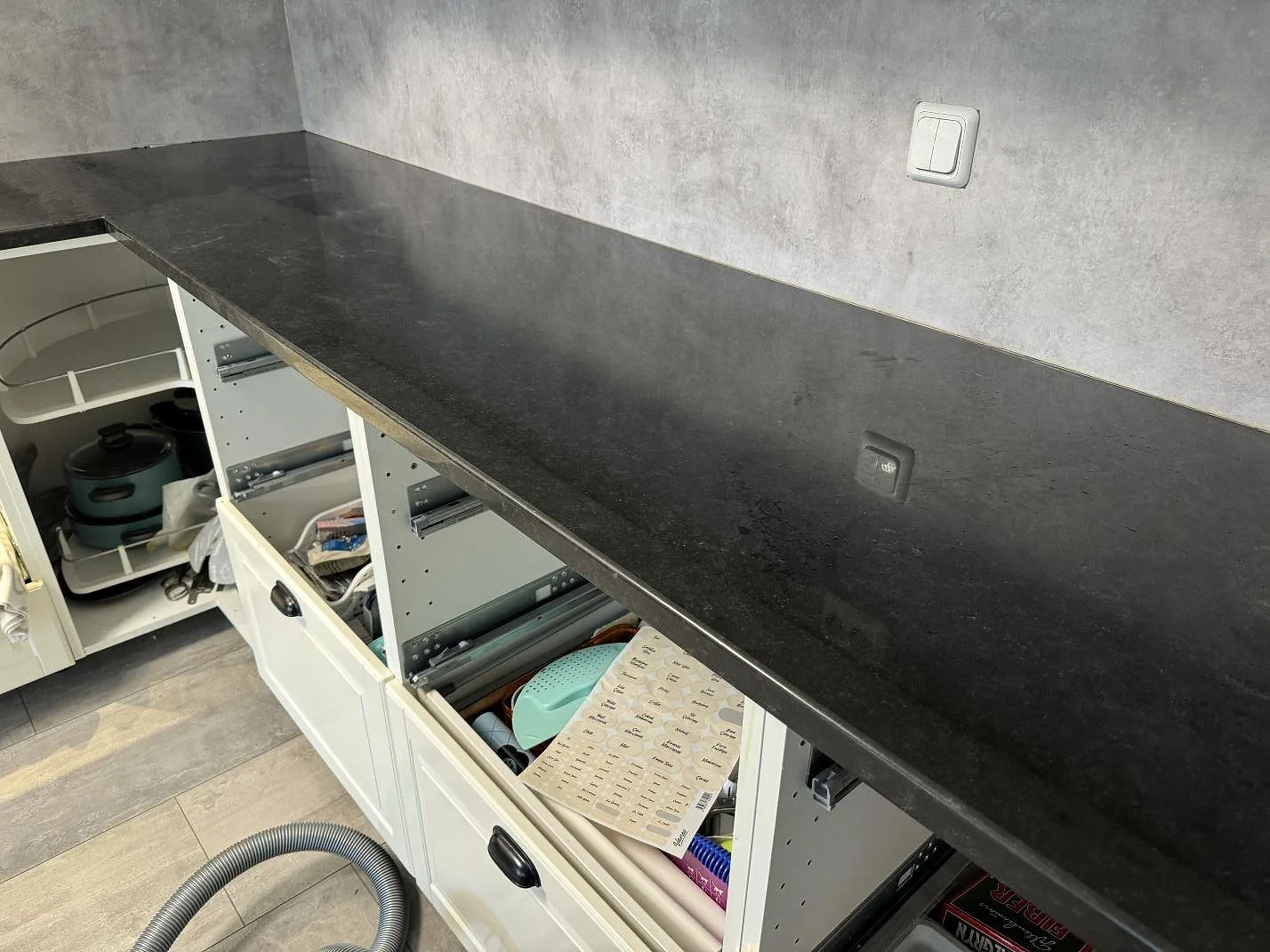 Lång bänkskiva i polerad Nero Assoluto granit längs vägg med betonglook och öppna vita stommar i Hyllinge.