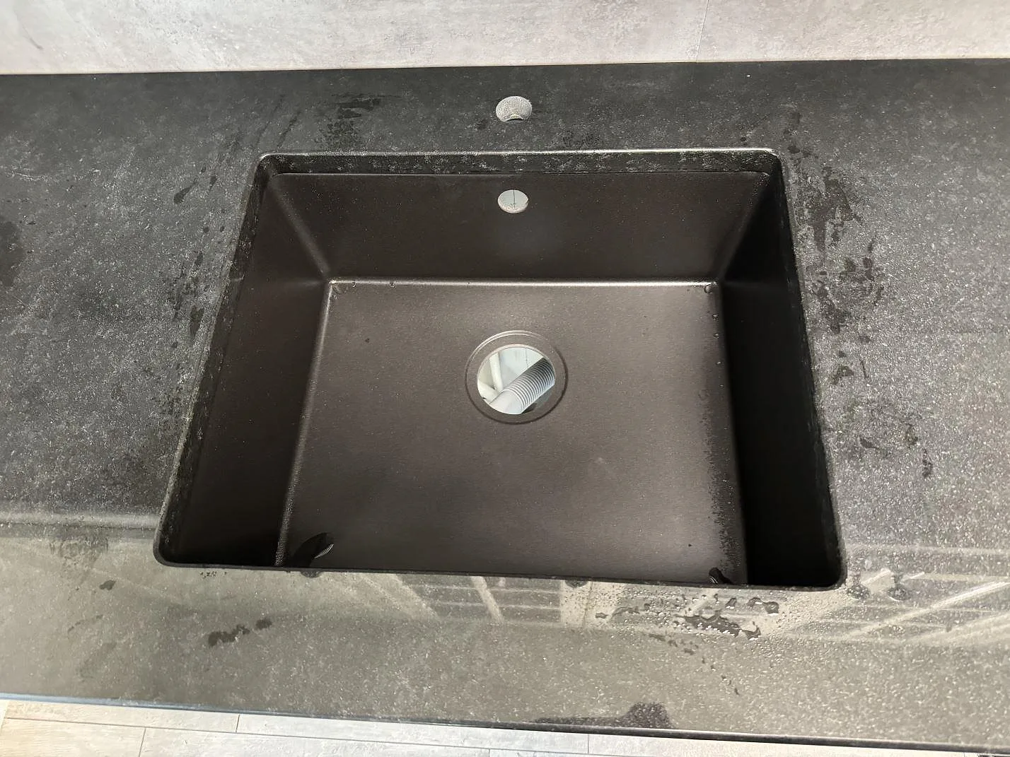 Närbild av svart diskho i polerad Nero Assoluto granit med kranhål och mörk stenyta i ett kök i Hyllinge.