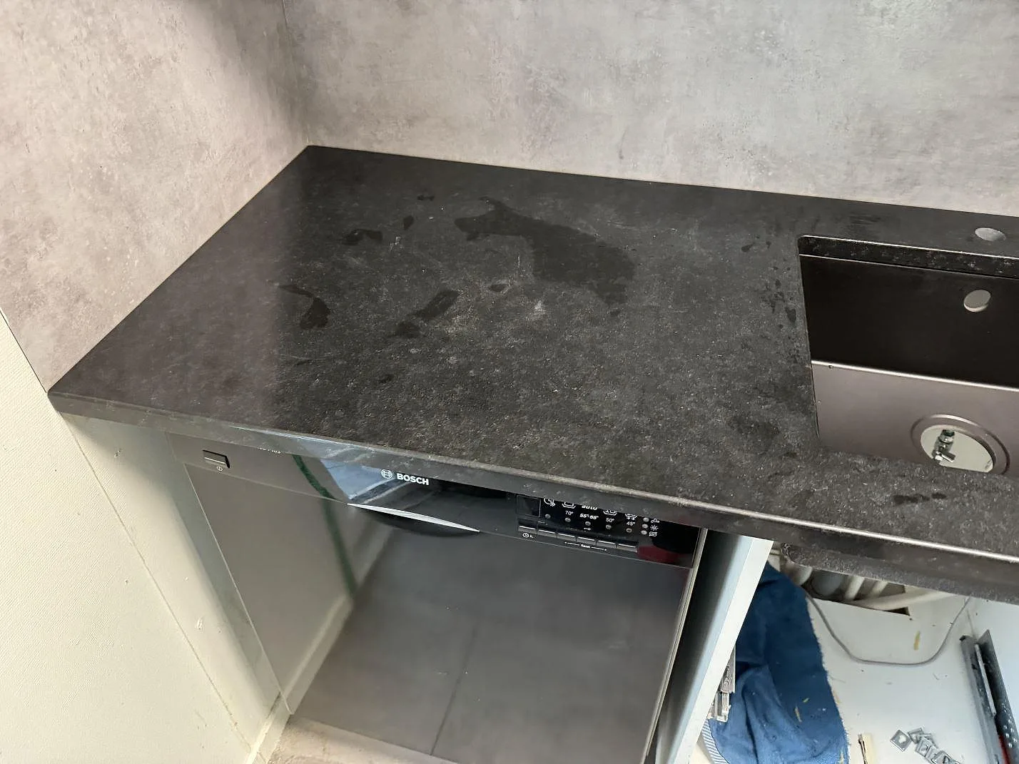 Polerad Nero Assoluto granit runt diskho och diskmaskin under montering i ett kök i Hyllinge.